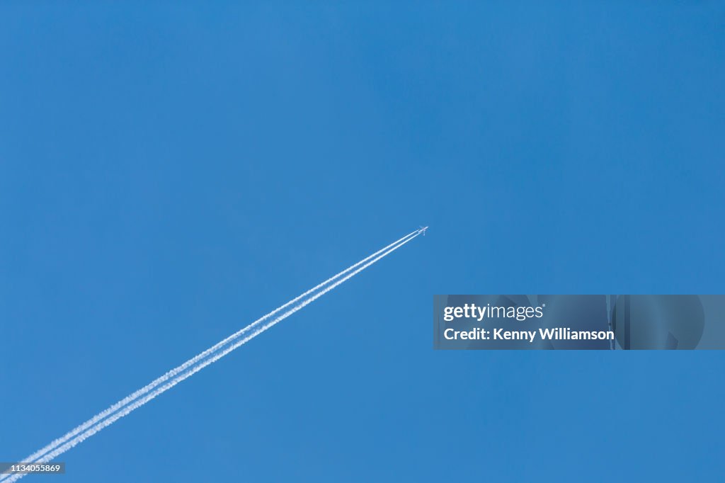 A distant jet aeroplane and vapour trails flying high in a clear blue sky