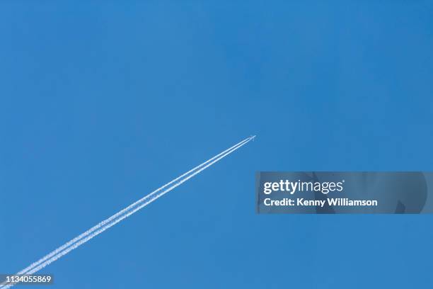 a distant jet aeroplane and vapour trails flying high in a clear blue sky - vapour trail stock pictures, royalty-free photos & images