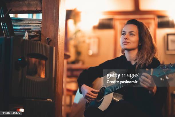 young woman playing guitar close up indoors in low light.playing guitar. young teeanger playing guitar by herself. - musician portrait stock pictures, royalty-free photos & images