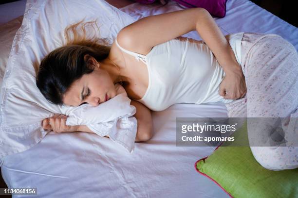 spansktalande ung kvinna som lider pms smärta i sängen - name tag bildbanksfoton och bilder