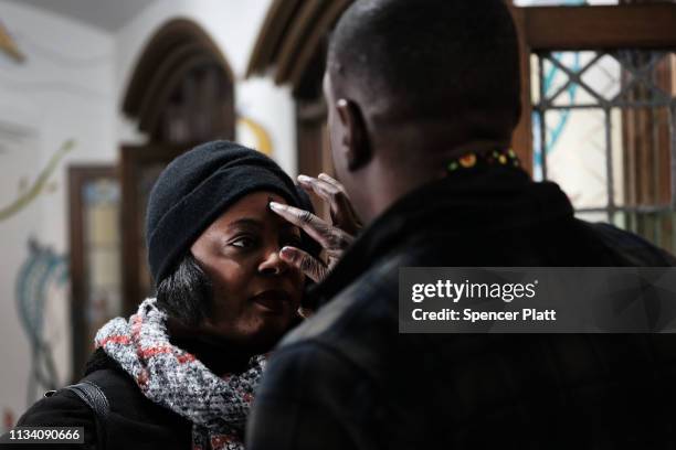 Roody Chatelain, a worshipper at the Church of the Village, administers a glitter ash cross on a forehead during a service at the historic church...