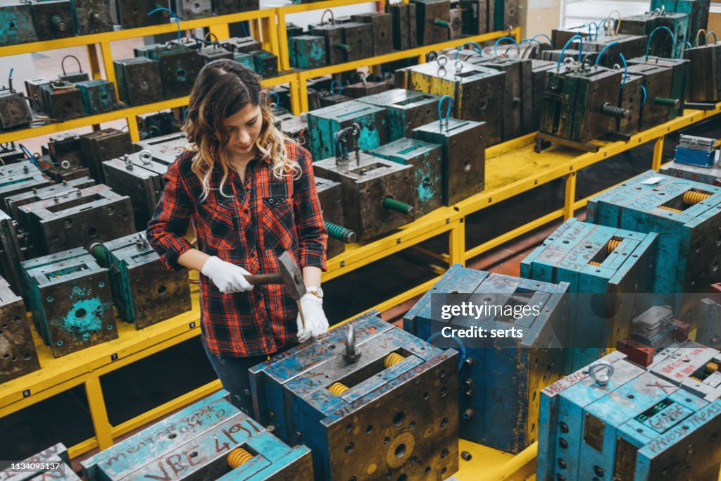Young woman working with hammer in industrial building