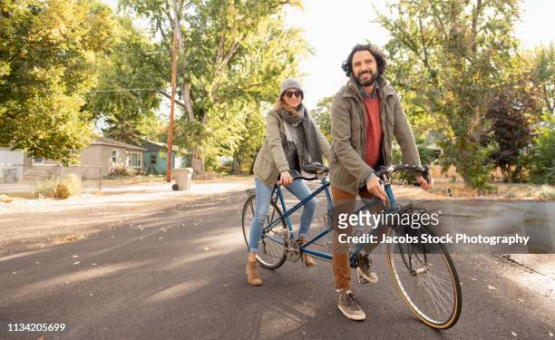 couple riding bicycles on suburban street - ciclismo tandem fotografías e imágenes de stock
