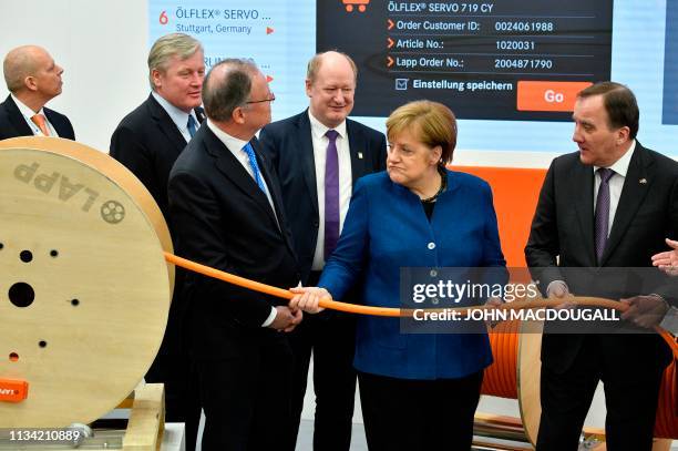 German Chancellor Angela Merkel and Swedish Prime Minister Stefan Lofven pull a cable that is fitted with a self-measuring app at the stand of Lapp...