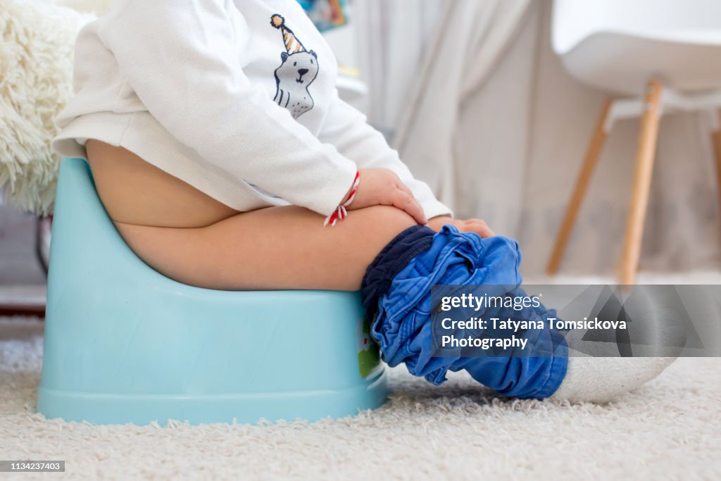 Children's legs in boots, hanging down from a chamber-pot on a home interior