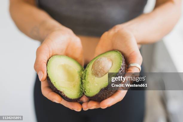 hands of woman holding halved avocado - avocado stock-fotos und bilder