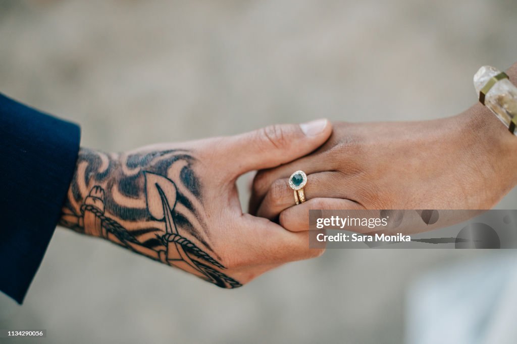 Bride and tattooed groom holding hands, cropped