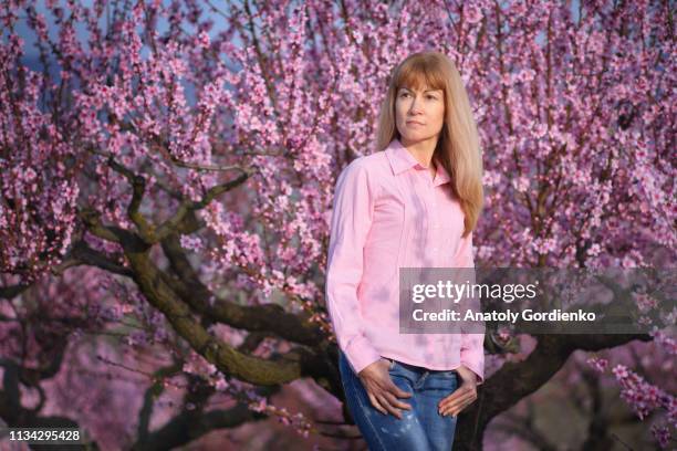 blonde with long hair in pink blouse on background of blooming garden, flowering peach trees. - woman pink dress stock pictures, royalty-free photos & images