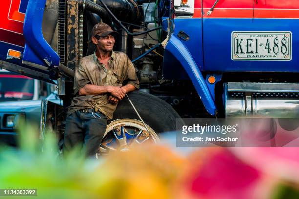 Colombian car mechanic leans against a truck wheel in Barrio Triste on December 6, 2017 in Medellin, Colombia. Barrio Triste is a working-class...