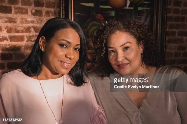 Two Latina moms looking at camera, sitting at dinner table.