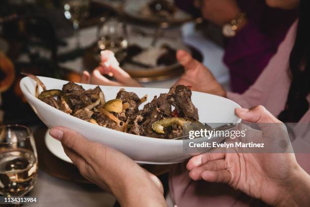Hands passing a serving bowl with peppered steak at a dinner table