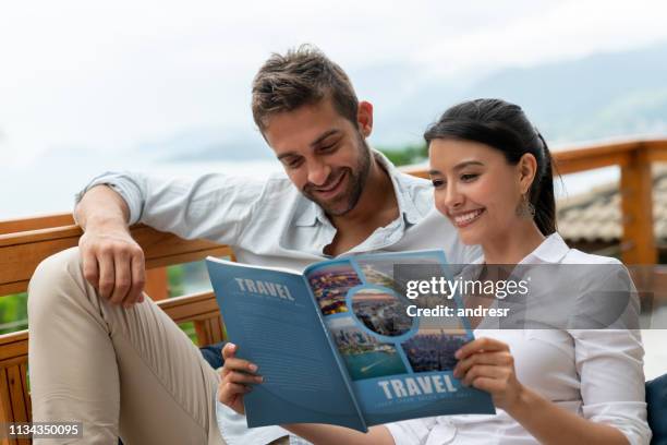 happy couple at home reading a travel magazine - magazine reading stock pictures, royalty-free photos & images