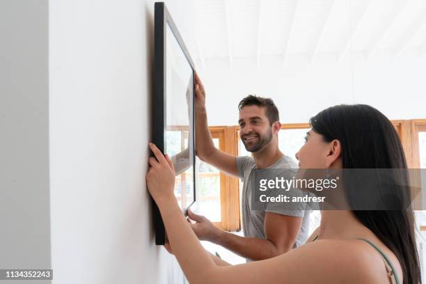 loving couple hanging a picture together at home - hanging stock pictures, royalty-free photos & images
