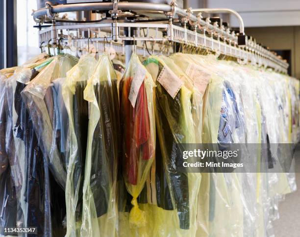 dry cleaning wrapped in plastic on rack - stomerij stockfoto's en -beelden