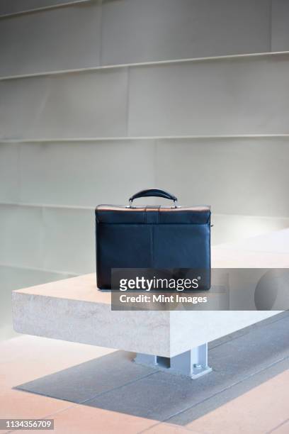 black briefcase on white stone bench - satchel bag stock-fotos und bilder