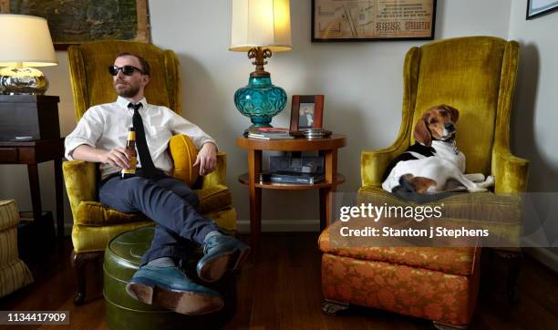 young man and pet dog relaxing in armchair in living room - well dressed dog stock pictures, royalty-free photos & images