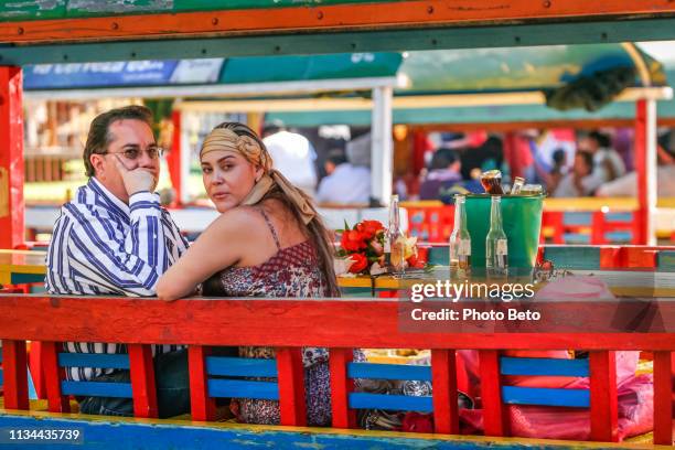 a couple aboard a colorful trajinera boat along the waters of lake xochimilco in southern mexico city - xochimilco stock pictures, royalty-free photos & images