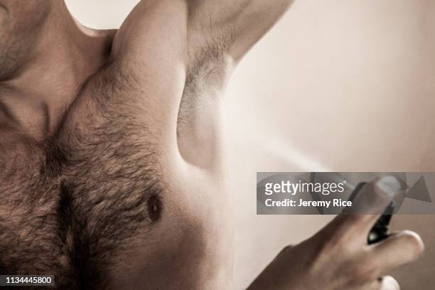 studio shot of mid adult man spraying deodorant - brusthaar stock-fotos und bilder