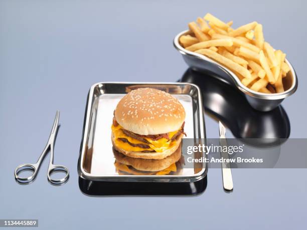 burger and fries sitting in surgical trays illustrating unhealthy diet - scalpel stockfoto's en -beelden