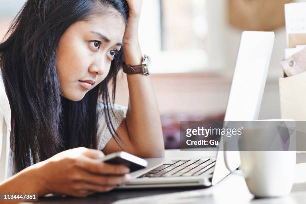 unhappy young woman sitting at desk with laptop and mobile phone - female worried mobile imagens e fotografias de stock