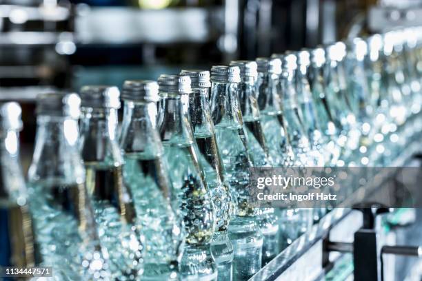 row of mineral water bottles on conveyor belt - bottling plant stock pictures, royalty-free photos & images