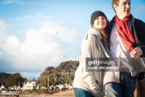 romantic couple out strolling at the coast - romantic couple walking winter beach stock pictures, royalty-free photos & images