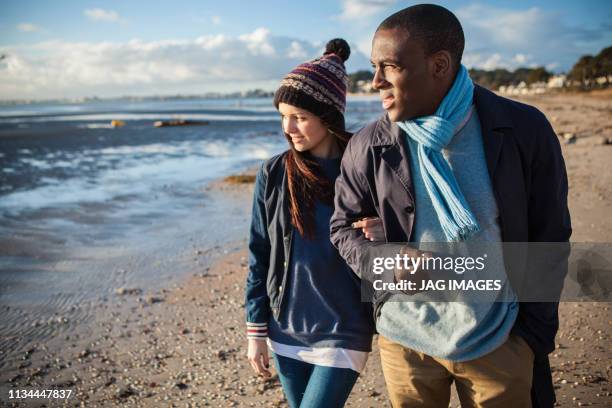 romantic young couple arm in arm on the beach - romantic couple walking winter beach stock-fotos und bilder