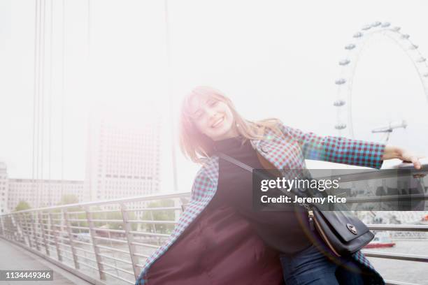 portrait of young female tourist swinging on golden jubilee footbridge, london, uk - millennium wheel stock pictures, royalty-free photos & images