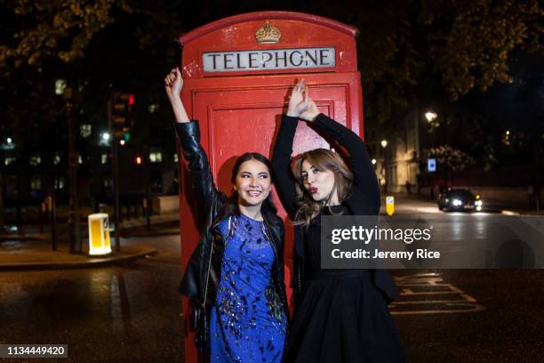 two young female friends dancing in front of red phone box at night, london, uk - red telephone box photos et images de collection