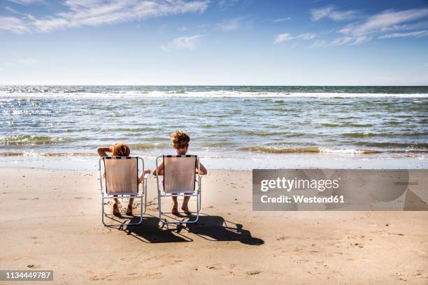 netherlands, zandvoort, boy and girl sitting on chairs on the beach - netherlands beach stock pictures, royalty-free photos & images