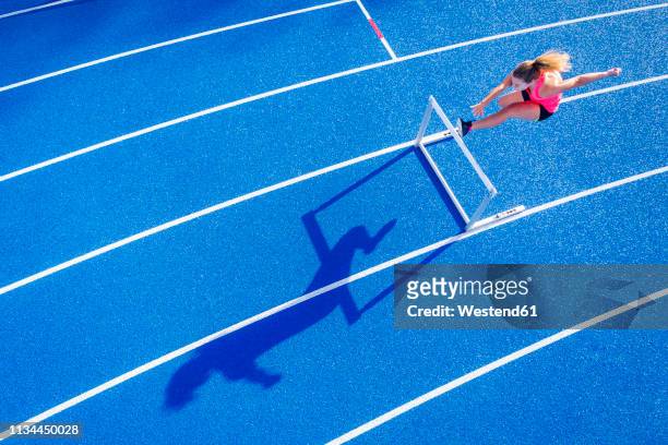 top view of female runner crossing hurdle on tartan track - leichtathletik stock-fotos und bilder