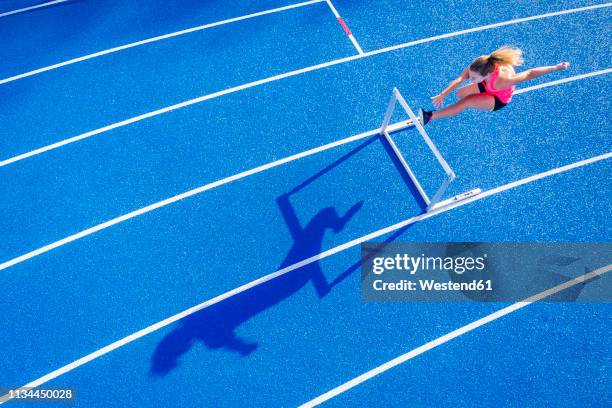 top view of female runner crossing hurdle on tartan track - hurdle stock pictures, royalty-free photos & images