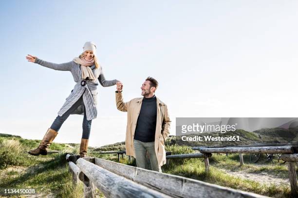 man helping woman balancing on wooden stakes in dunes - couple dunes stockfoto's en -beelden