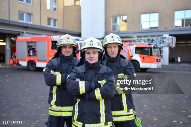 portrait of three confident firefighters standing on yard in front of fire engine - feuerwehr deutschland stock-fotos und bilder