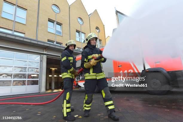 two firefighters standing on yard exercising with extinguishing water - extinguishing stockfoto's en -beelden