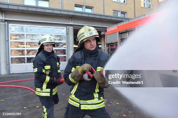 two firefighters standing on yard exercising with extinguishing water - feuerwehr deutschland stock-fotos und bilder