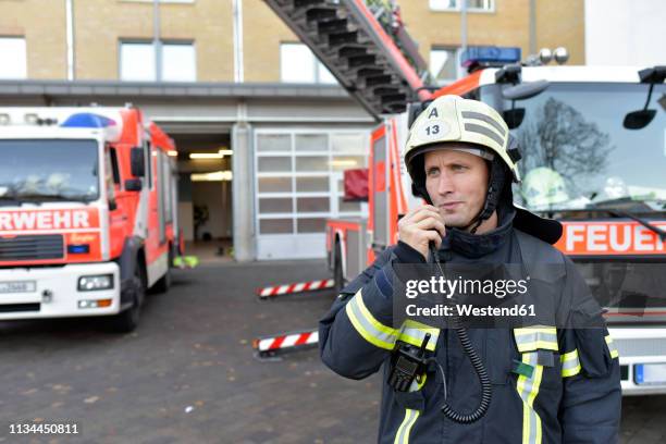 firefighter standing on yard at fire engine using walkie talkie - vehículo de emergencia fotografías e imágenes de stock