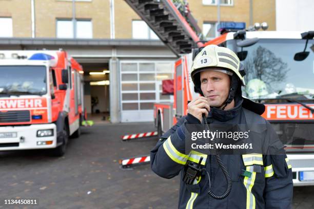 firefighter standing on yard at fire engine using walkie talkie - carro de bombeiro - fotografias e filmes do acervo