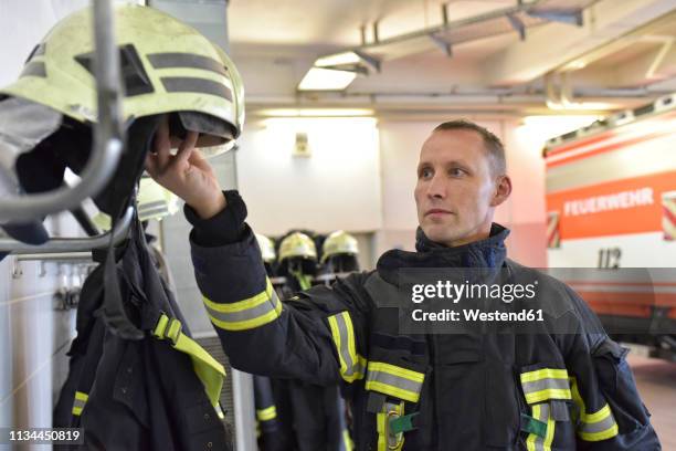 firefighter taking helmet from rack in fire station - fire station - fotografias e filmes do acervo