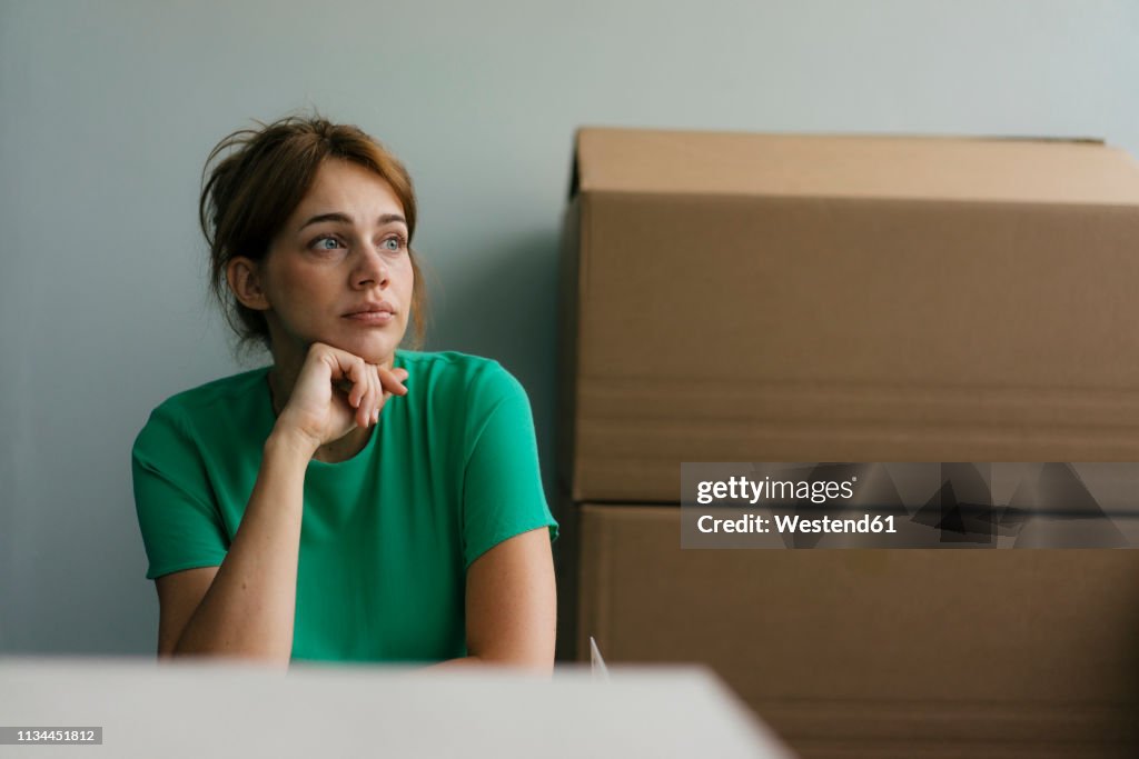 Thoughtful woman next to cardboard boxes in office