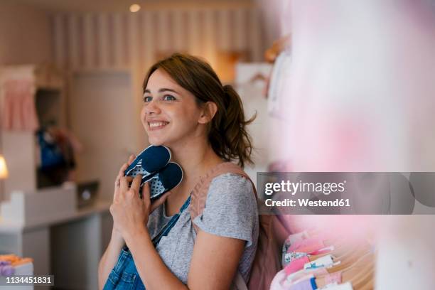 smiling pregnant woman shopping for baby clothing in a boutique - baby clothes stock pictures, royalty-free photos & images