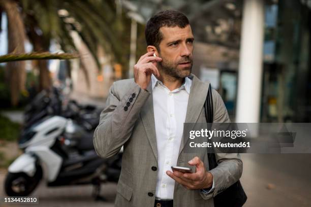 businessman with cell phone in the city applying earbuds - ohrhörer stock-fotos und bilder