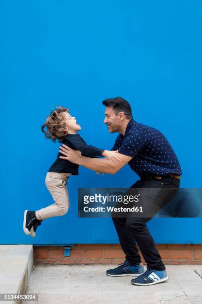 happy father playing with son at blue wall - jump dad stockfoto's en -beelden