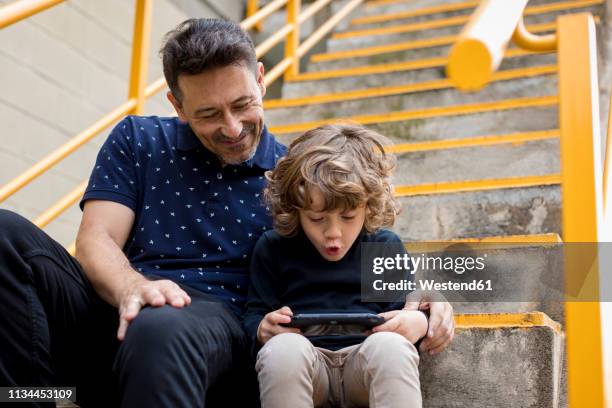 father watching son playing with handheld game console - game console stockfoto's en -beelden