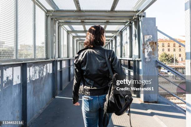 rear view of young woman walking on a bridge - chaqueta de cuero fotografías e imágenes de stock