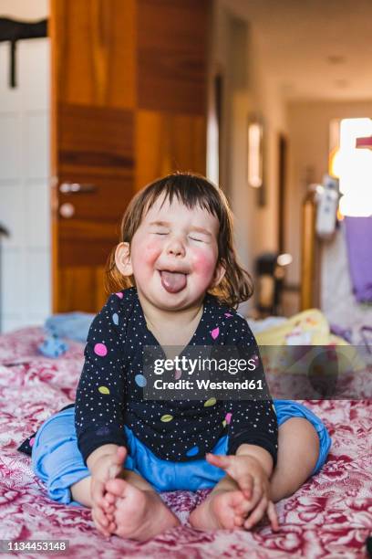 portrait of toddler sitting barefoot on bed sticking out tongue - rosy cheeks stock pictures, royalty-free photos & images