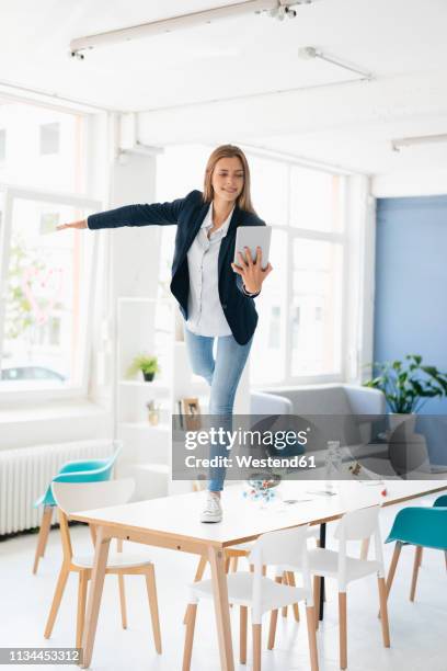 young businesswoman balancing on one leg on desk in the board room, holding digital tablet - pretending to be a plane stock pictures, royalty-free photos & images