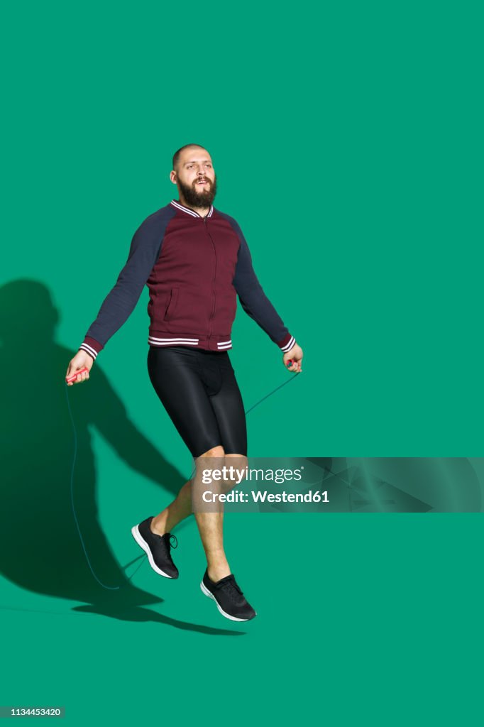 Portrait of bearded man skipping rope in front of green backgrpund