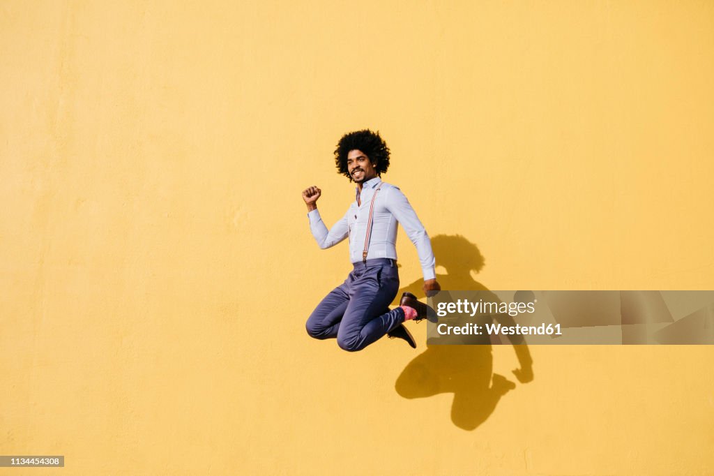 Smiling man jumping in the air in front of yellow wall