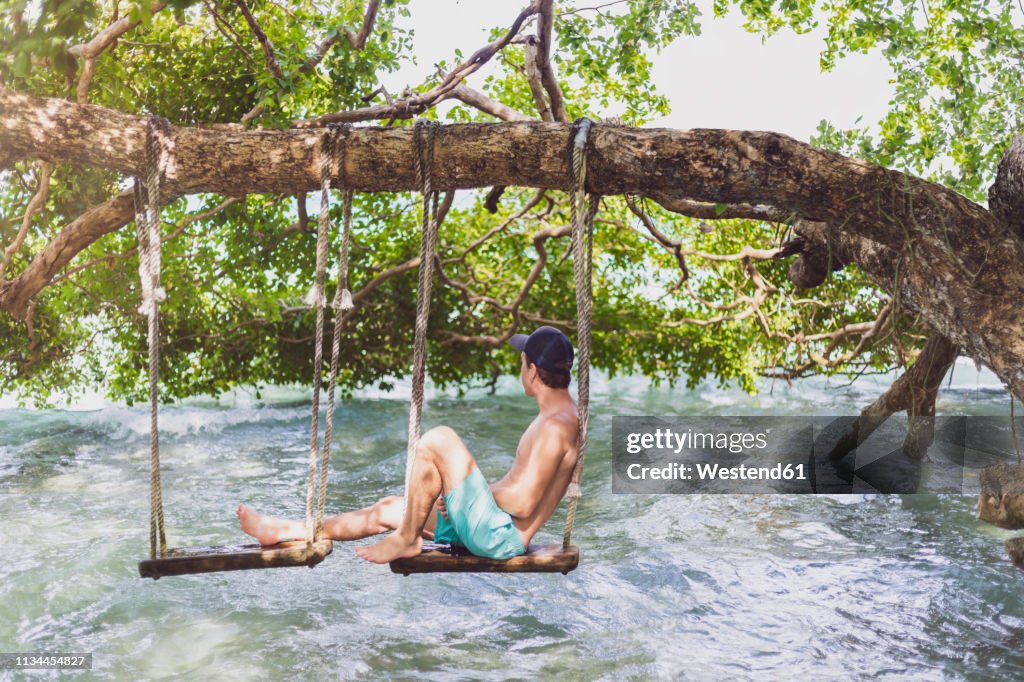 Mexiko, Yucatan, Quintana Roo, lagoon of Bacalar, man sitting on tree swing above the water